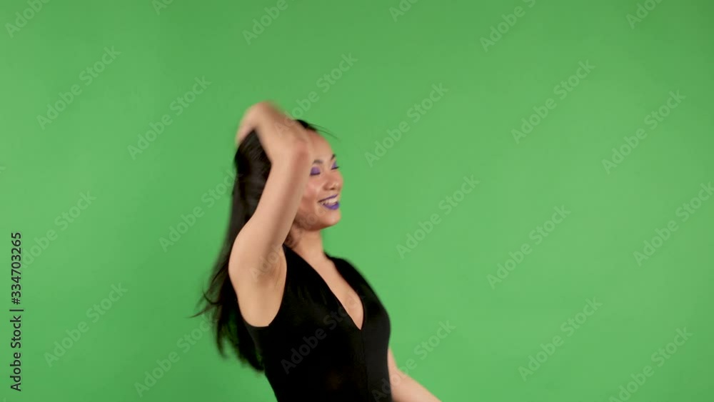 Energetic happy young asian woman smiling and dancing against green background throwing up her long black hair with her hands Energetic happy young asian woman smiling and dancing against green background throwing up her long black hair with her hands
