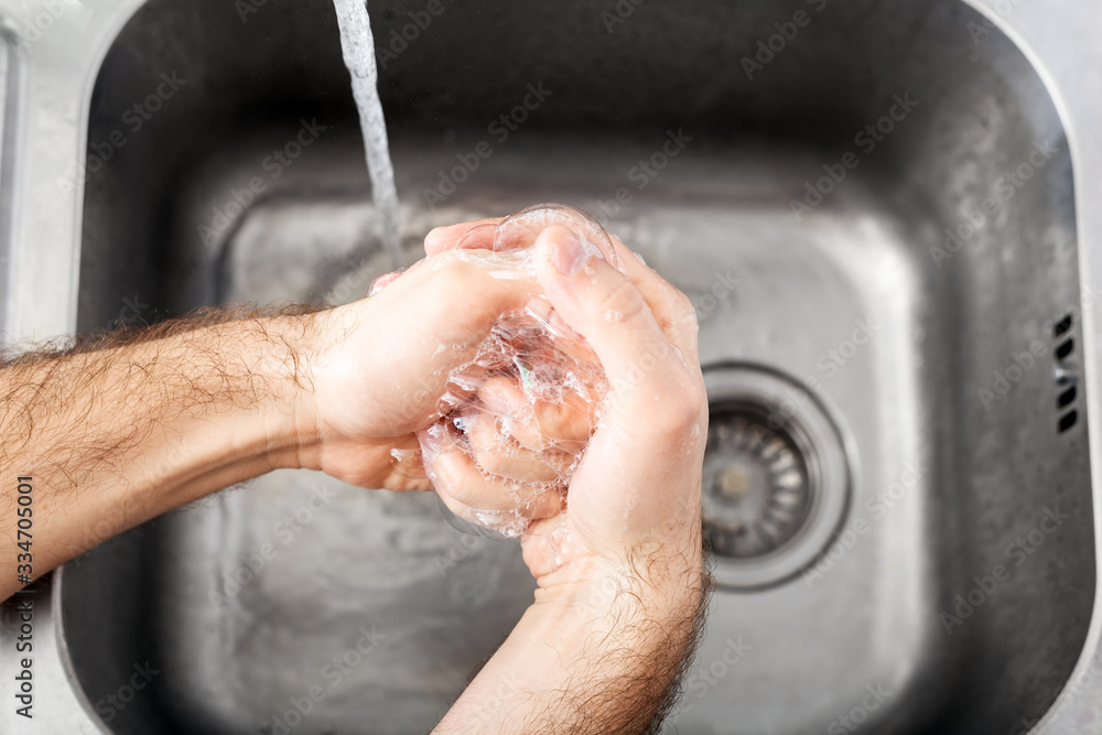 Fototapeta premium Man washing hands with antibacterial soap and water in metal sink for corona virus prevention. Hand hygiene, health care, medical concept. Hand skin disinfection protect from Coronavirus covid 19