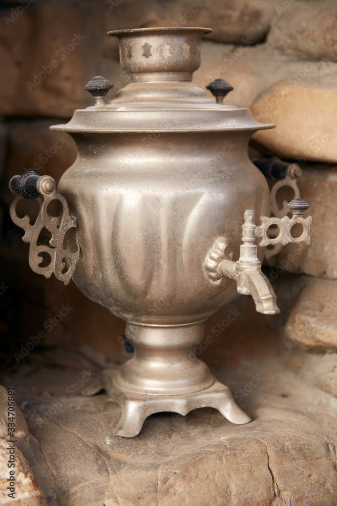 The silver samovar stands in a stone niche. An old iron samovar stands in the house during the day The silver samovar stands in a stone niche. An old iron samovar stands in the house during the day