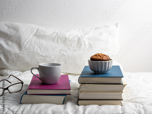 Eine Tasse Kaffee und ein Muffin auf einem Buchstapel im Bett, Frühstück, Soziale Distanz photo