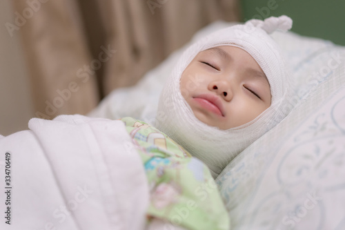 Little asian girl lying sick with bandaged head on bed at hospital. Baby girl injury and headache.
