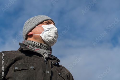 Disease outbreak, coronavirus covid-19 pandemic. Close up portrait from below of a man posing outdoors protecting his face with a mask © cineberg