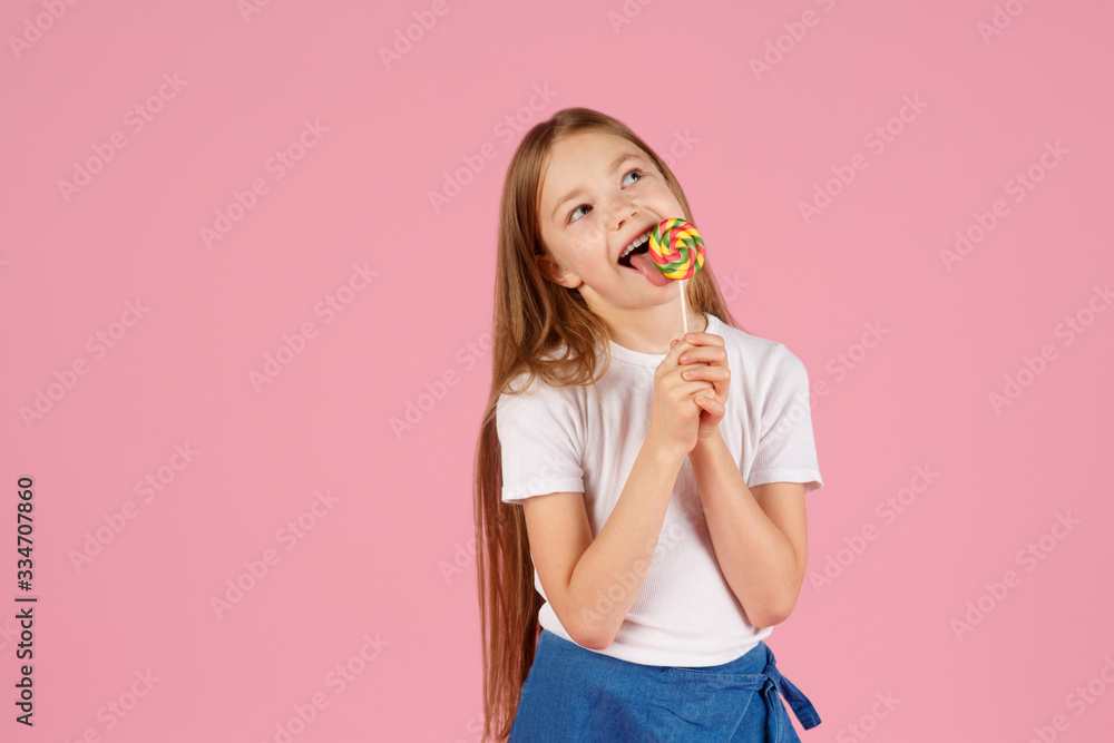 Portrait of a surprised little girl holding heart shaped lollipop and looking at camera isolated over pink background. Portrait of a surprised little girl holding heart shaped lollipop and looking at camera isolated over pink background.