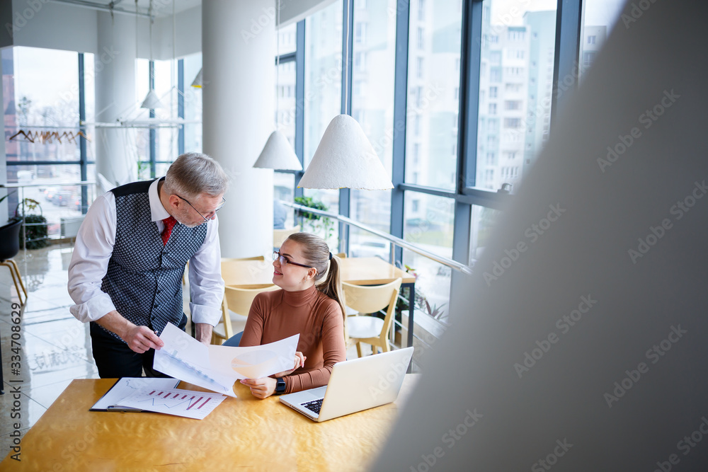 Fototapeta premium Girl business lady sitting at a wooden table with a laptop and discussing a new project with her boss mentor teacher. New business development concept
