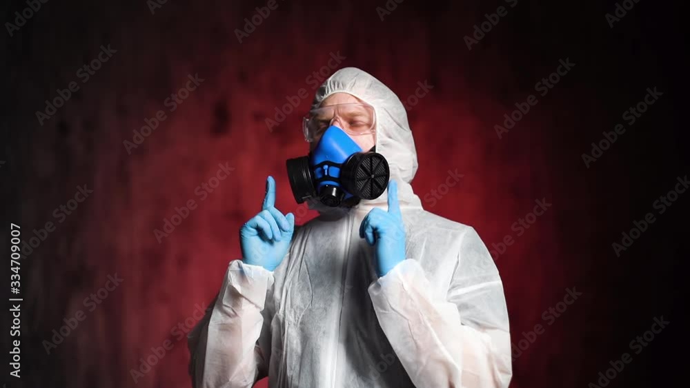 Relaxed man-medic wearing protective suit, goggles and a respirator dances. Concept of Coronavirus COVID-19 Pandemic. Studio shot in slow motion on isolated sinister dark red background. Relaxed man-medic wearing protective suit, goggles and a respirator dances. Concept of Coronavirus COVID-19 Pandemic. Studio shot in slow motion on isolated sinister dark red background.
