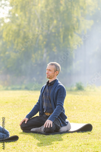 A young man meditates outdoors in a park. 