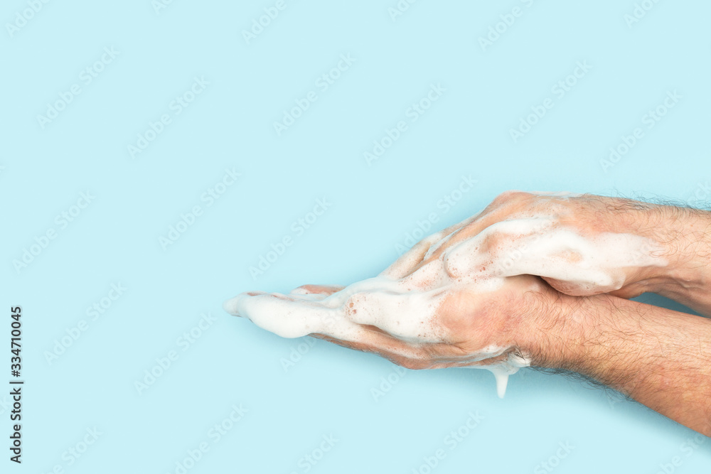 Manos de hombre con jabón espuma sobre un fondo celeste liso aislado. Vista de frente. Copy space