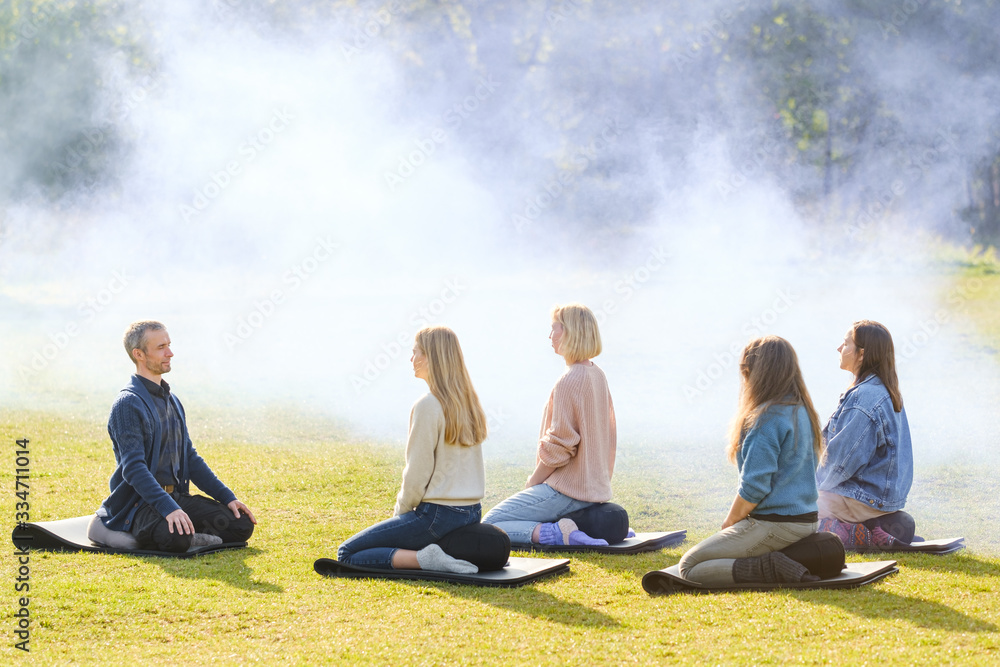 A group of young people meditate outdoors in a park. A group of young people meditate outdoors in a park.