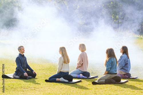 A group of young people meditate outdoors in a park. 