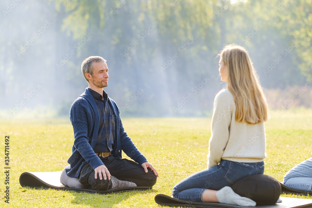 A group of young people meditate outdoors in a park. A group of young people meditate outdoors in a park.
