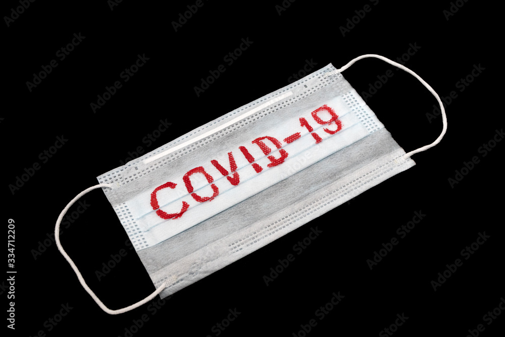 Isolated medical face mask with a ''COVID-19'' title against a black background Isolated medical face mask with a ''COVID-19'' title against a black background