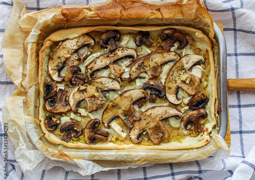 Mushroom tart baked in a metal tray and served on a wooden board. Healthy and crunchy veggie tart on marble table. 