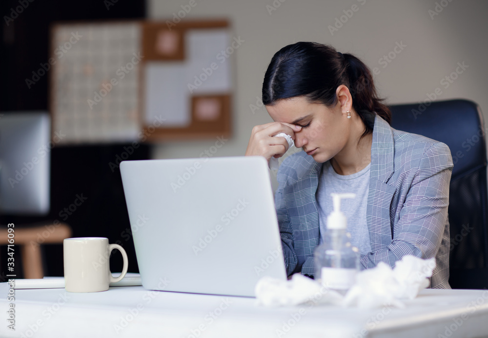 Sick, ill unhealthy female employee working in workplace in office and wearing surgical hygienic mask on her face. Concept of corona virus or covid-19 Sick, ill unhealthy female employee working in workplace in office and wearing surgical hygienic mask on her face. Concept of corona virus or covid-19