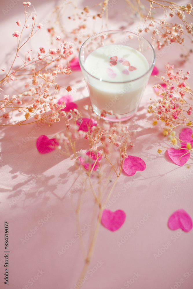 Glass with milk on a pink background with heart shaped confetti Glass with milk on a pink background with heart shaped confetti