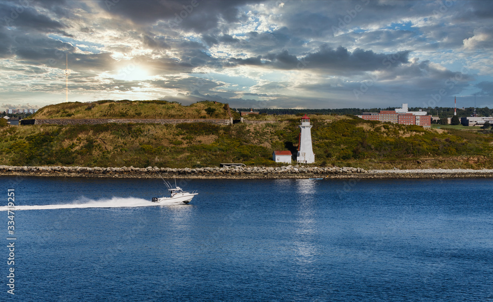 A white speedboat in blue water approaching a white lighthouse