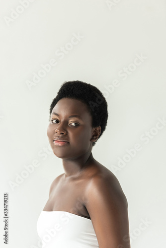 attractive smiling african american girl in white top isolated on grey