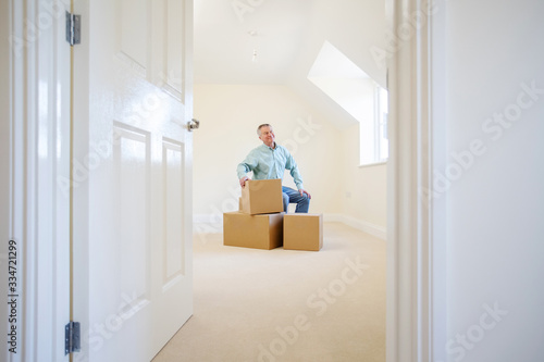 Senior Man Downsizing In Retirement Sitting On Boxes In New Home On Moving Day