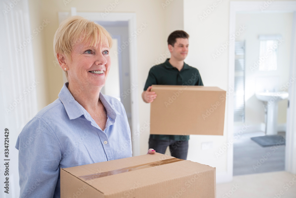 Senior Woman Downsizing In Retirement Carrying Boxes Into New Home On Moving Day With Removal Man Helping Senior Woman Downsizing In Retirement Carrying Boxes Into New Home On Moving Day With Removal Man Helping