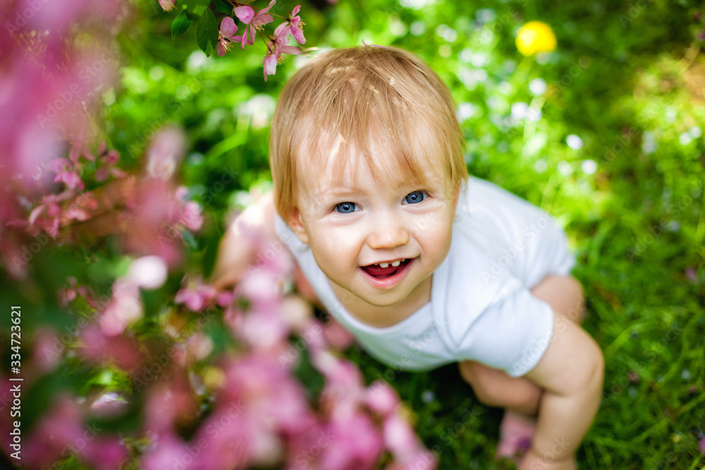 Close-up portrait of a 1-2 year old girl outdoors in a garden with pink flowers in the trees. Close-up portrait of a 1-2 year old girl outdoors in a garden with pink flowers in the trees.