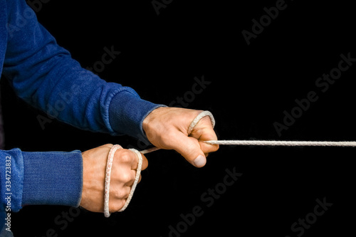 Hands with a rope on a black background. A man pulls a sports rope.