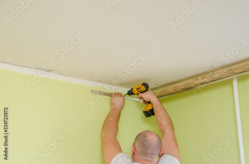 Fastening to the wall guide for stretch ceiling. Repairers make installation of a stretch ceiling