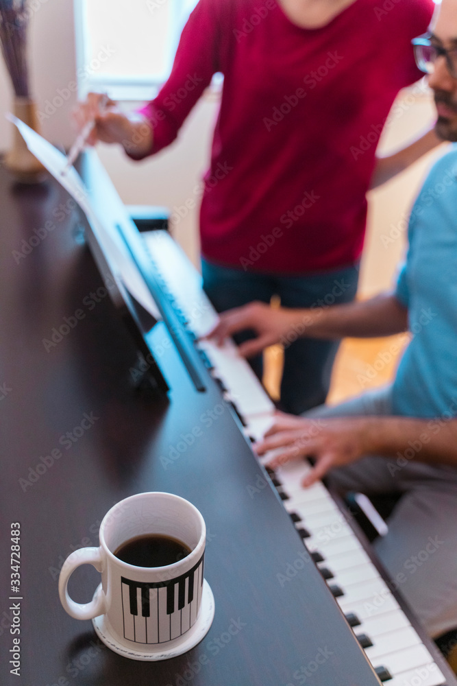 Vertical detail of teacher explaining classical keyboard morning class with coffee at home. Student practicing index hands on musical instrument. Unrecognizable man learning piano lessons at home.