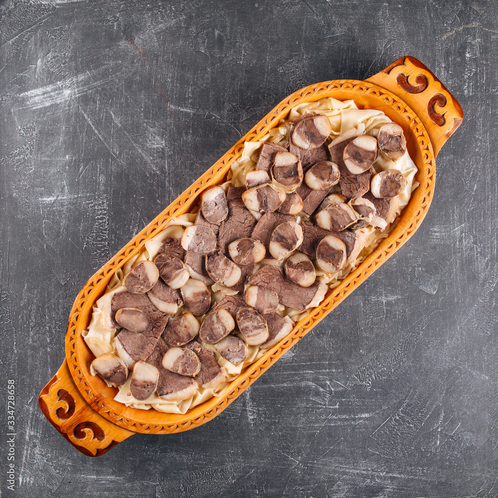 Kazakh national dish Beshbarmak on a wooden traditional plate, top view, square format, Central Asian cuisine Kazakh national dish Beshbarmak on a wooden traditional plate, top view, square format, Central Asian cuisine