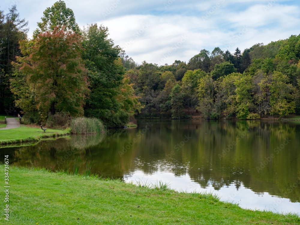 Fototapeta premium Twin Lakes in the Laurel Highlands of Pennsylvania with the tree line reflecting in the water, grass foreground and blue sky with clouds in the background. Beautiful scenic nature landscape.