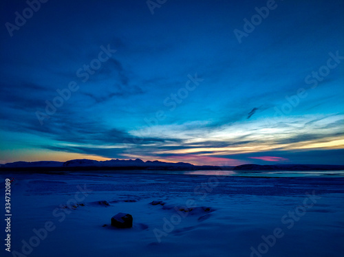 Enjoying the sunrise with this great combination of colours such us blue, red and yellow  a frozen lake as a background and surrounded by mountains © andres