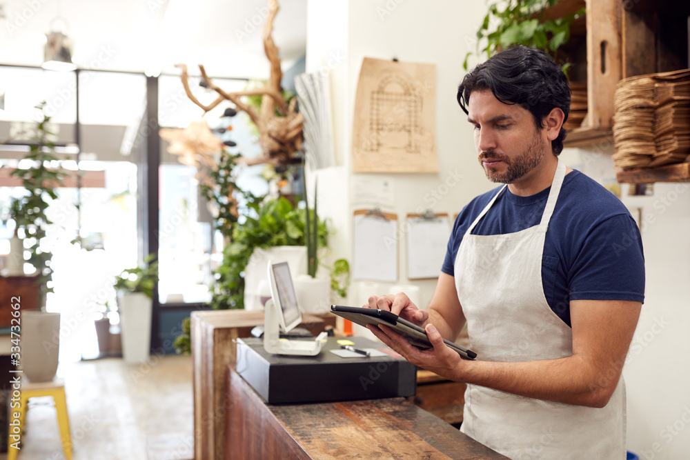 Male Owner With Digital Tablet Standing Behind Sales Desk Of Florists Store Male Owner With Digital Tablet Standing Behind Sales Desk Of Florists Store