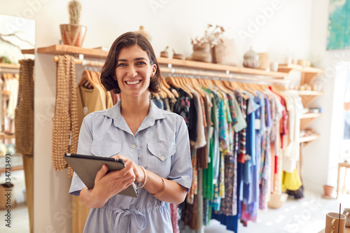 Portrait Of Female Owner Of Fashion Store Checking Stock In Clothing Store With Digital Tablet photo