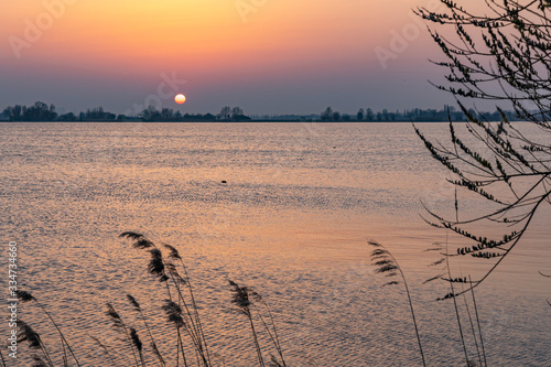 The setting sun almost disappears behind the shore of Lake Zoetermeerse Plas in Zoetermeer  The Netherlands