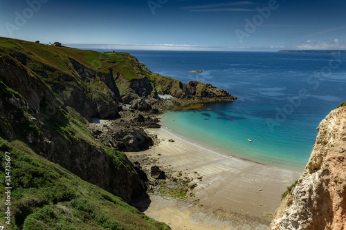 Coast and beach during sunny day with blue and turquoise waters surrounded by green and rocky cliffs in Sark, Guernsey, Channel Islands, United Kingdom