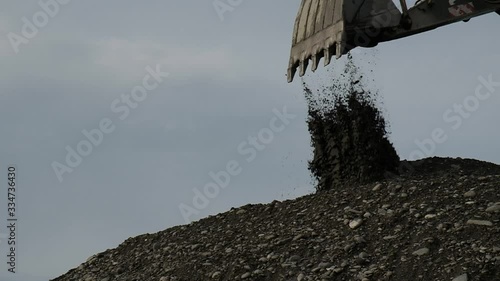The excavator works with an arrow and a bucket. Moves black sand at a construction site.