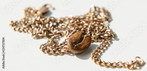 On a white background lies a gold chain. On a gold chain lies coffee bean. Close-up. Concept - precious coffee, coffee lovers, choose coffee.