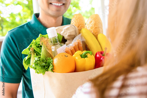 Smiling delivery man giving grocery bag to woman customer at home for online food shopping service concept