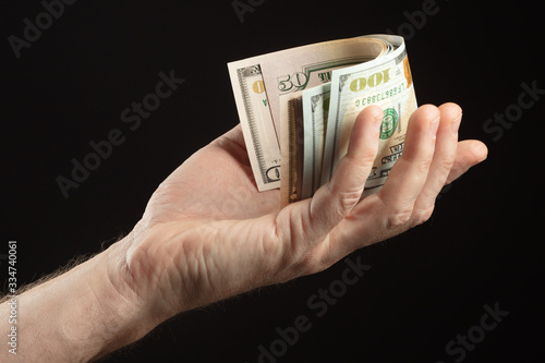 A pile of American currency (or dollars) folded in half in a man’s hand on a black background. Investing management and saving concept. Selective focus