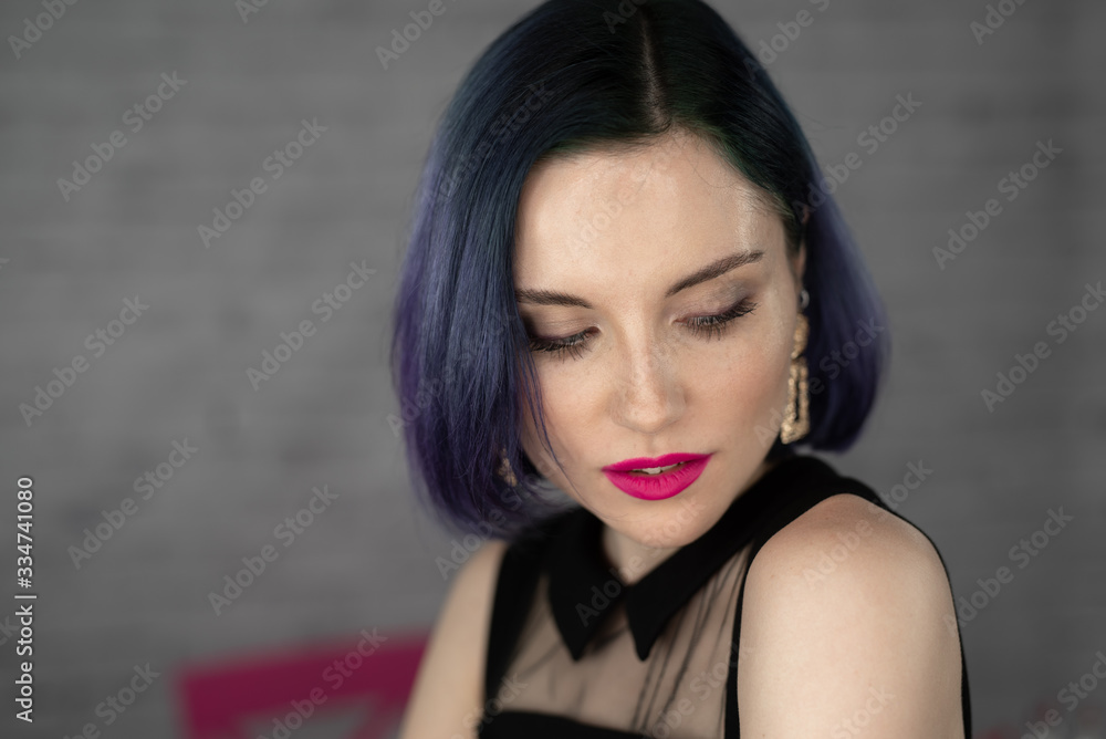 Young beautiful girl with professional makeup, blue hair and perfect skin sits in studio in front of ring light lamp posing for social media. Beauty blog. Copy space. Young beautiful girl with professional makeup, blue hair and perfect skin sits in studio in front of ring light lamp posing for social media. Beauty blog. Copy space.