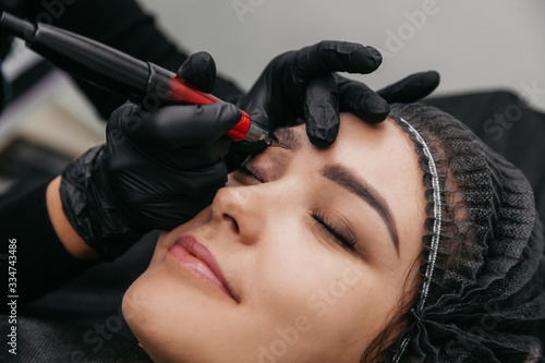 Girl master beautician makes eyebrow tattoo