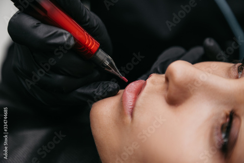 Girl professional master beautician makes lip tattoo on a pigment. Macro close-up shot
