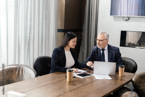 smiling businessman and asian businesswoman talking during business meeting