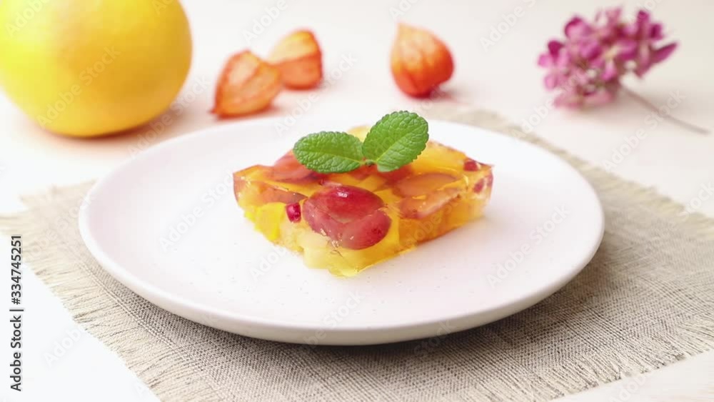 Male hand decorate fruit jelly with mint on a white ceramic plate. Side view, close up. Male hand decorate fruit jelly with mint on a white ceramic plate. Side view, close up.