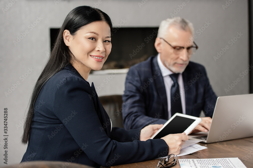 selective focus of smiling asian businesswoman with digital tablet and businessman on background selective focus of smiling asian businesswoman with digital tablet and businessman on background