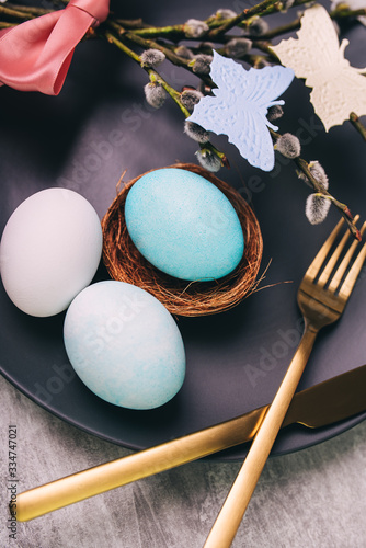 Easter table setting with grey plate and blue egg in nest on grey wooden table, close-up.