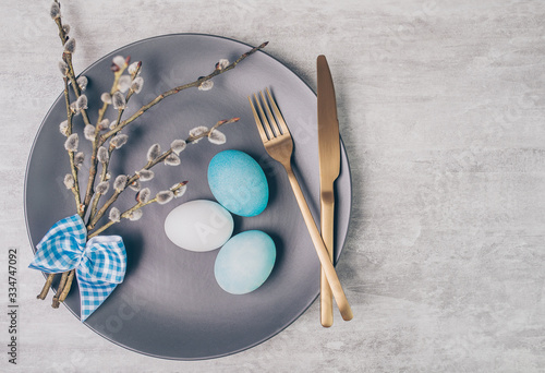 Easter table setting with grey plate and blue eggs on grey table. Top view.