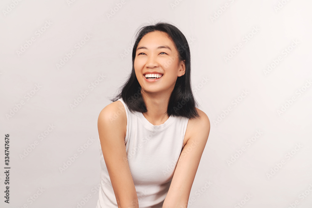 Girl cackles and looks up at empty space for text and your ad. Beautiful young woman Asian appearance with black hair brown eyes stands isolated white background in Studio Girl cackles and looks up at empty space for text and your ad. Beautiful young woman Asian appearance with black hair brown eyes stands isolated white background in Studio