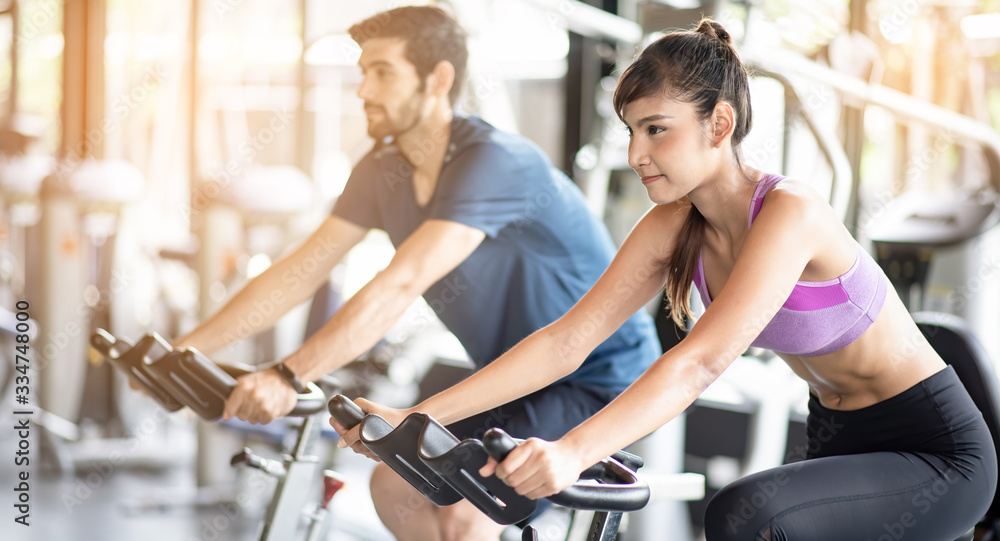 Young asian healthy woman bike cardio at the gym with smile and fresh face with her friend. Exercise, workout, muscle training, weight lifting, weight loss, heart rate practice and diet concept. Young asian healthy woman bike cardio at the gym with smile and fresh face with her friend. Exercise, workout, muscle training, weight lifting, weight loss, heart rate practice and diet concept.