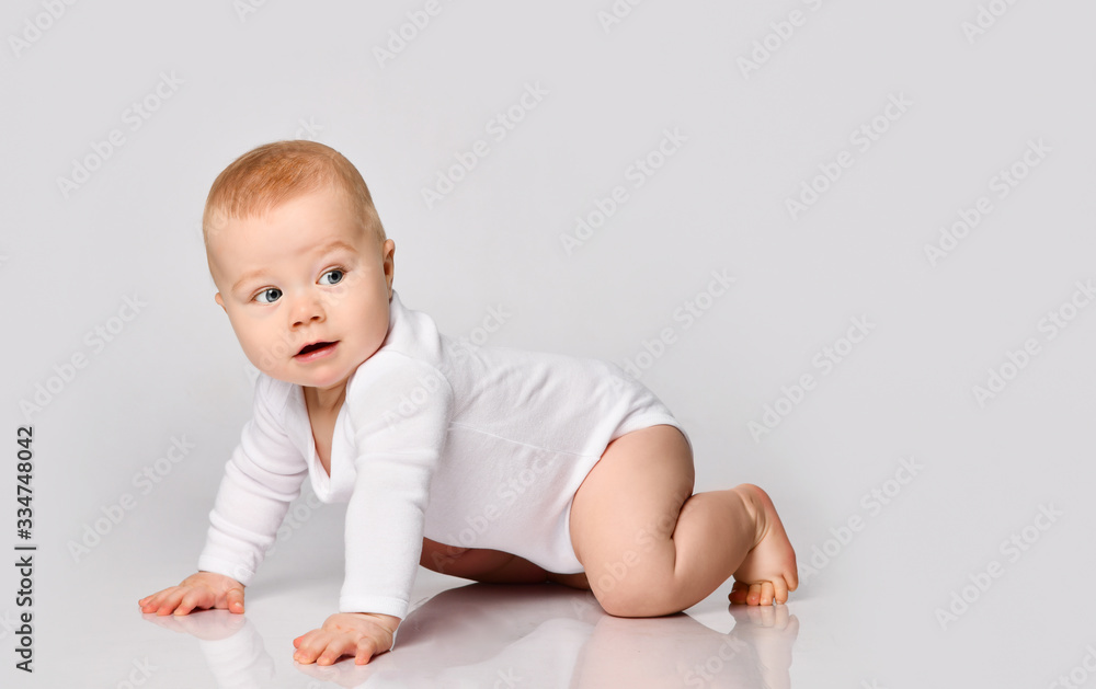 Chubby ginger little one in bodysuit, barefoot. He is sitting on floor isolated on white studio background. Close up, copy space Chubby ginger little one in bodysuit, barefoot. He is sitting on floor isolated on white studio background. Close up, copy space