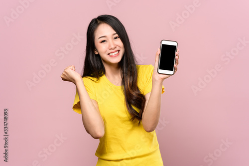Fotografija Portrait photo of young beautiful Asian woman feeling happy or surprise shock and holding smart phone with black empty screen on pink background can use for advertising or product presenting concept