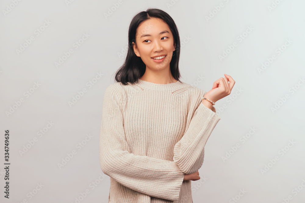 Coquettishly girl looks away at place of your advertisement. young woman Asian appearance with black hair and brown eyes dressed in knitted warm sweater stands isolated white background in Studio Coquettishly girl looks away at place of your advertisement. young woman Asian appearance with black hair and brown eyes dressed in knitted warm sweater stands isolated white background in Studio